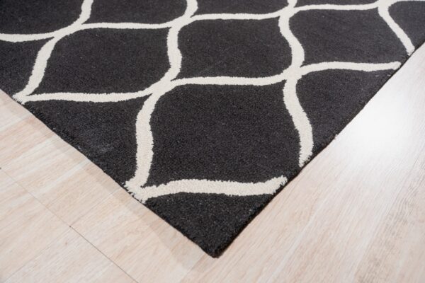 Textured charcoal rug with raised white geometric lines lies on light wood planks.