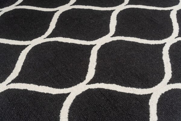 Black rug with a thick, off-white, textured looping geometric pattern in close detail.
