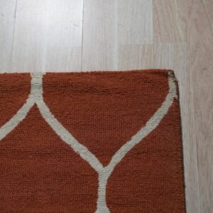A close-up view of an orange loop pile rug with a white trellis pattern on light wood flooring.