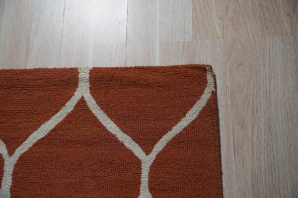 A close-up view of an orange loop pile rug with a white trellis pattern on light wood flooring.
