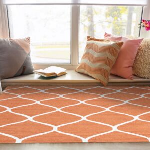 Low-pile orange and white trellis rug on a light wood floor in a bright window nook.