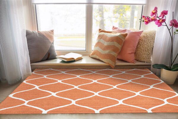 Low-pile orange and white trellis rug on a light wood floor in a bright window nook.