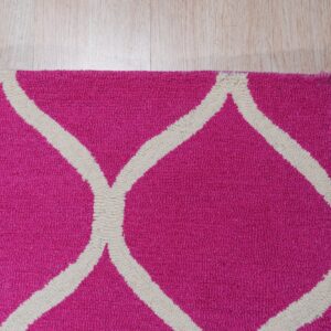A textured pink rug with an off-white geometric trellis pattern is shown resting on light wood flooring.