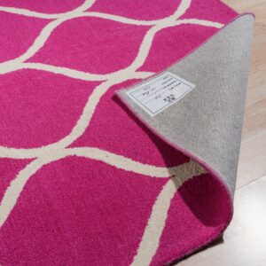 A curled magenta and off-white geometric pattern rug with a tag, exposing the backing on light wood flooring.