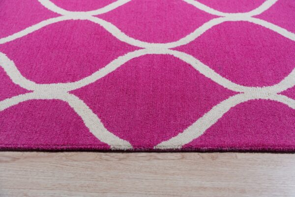 Close-up of a pink textured rug with a thick white trellis pattern on light wood flooring.