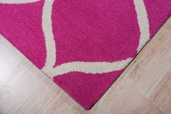 A magenta and cream geometric rug with visible loop texture rests on light wood plank flooring.
