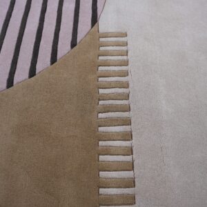 Geometric rug close-up showing pink stripes, solid brown fields, and alternating carved beige and brown textural segments.