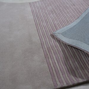 Pink and taupe rug showing smooth and textured striped areas, folded back to reveal the tightly woven backing.