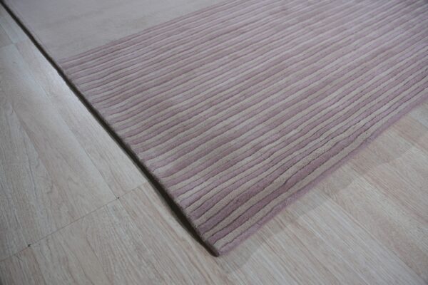 Close-up of a high-pile rug with carved mauve and pale beige diagonal stripes on light wood flooring.