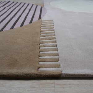 Abstract carved rug featuring dimensional stripes and color blocks in tan, mauve, and light gray on a wood floor.