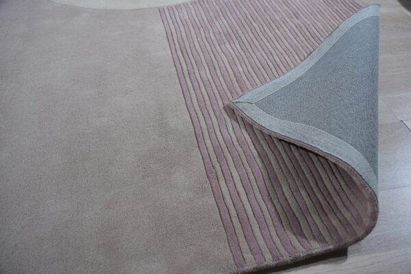 Low-pile rug in taupe and mauve vertical stripes, corner folded back revealing the gray fabric backing.