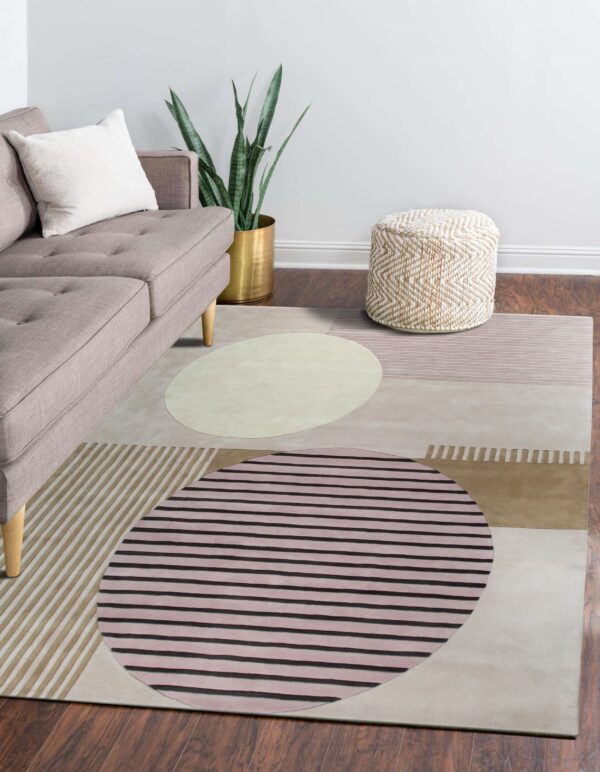 A modern rug featuring large abstract circles and stripes in beige, pink, and taupe colors on dark wood flooring.