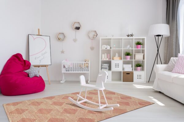 A peach and cream flatwoven rug with a geometric diamond pattern is centered in a bright white nursery.
