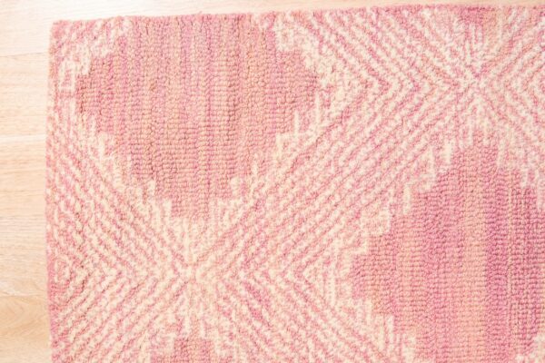 Textured pink and ivory loop-pile rug displaying a geometric pattern rests on light wooden flooring.