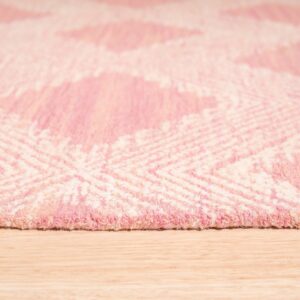 A thick, pink and cream rug featuring a large geometric diamond pattern rests on light wood planks.