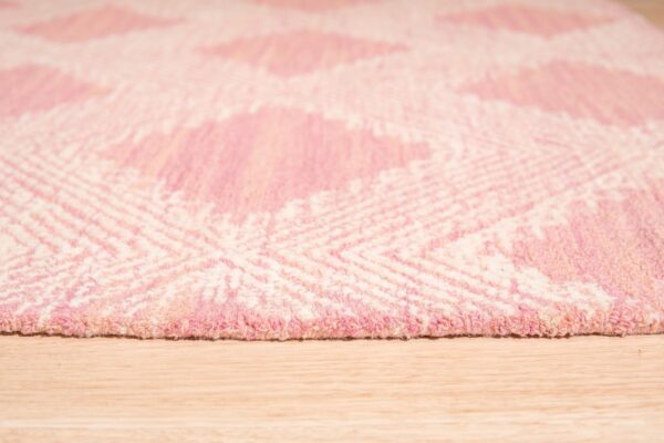 A thick, pink and cream rug featuring a large geometric diamond pattern rests on light wood planks.