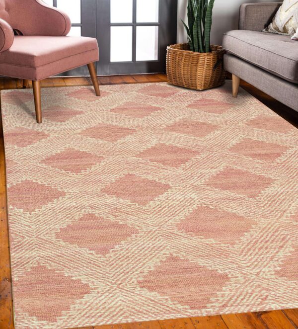 A dusty pink geometric rug lies on hardwood flooring between a pink armchair and a gray couch.