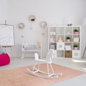 Low-pile coral rug with white concentric line patterns anchors a nursery with a crib and rocking horse.