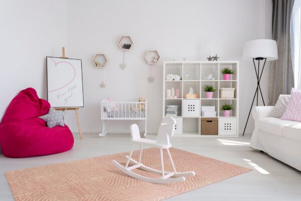 Low-pile coral rug with white concentric line patterns anchors a nursery with a crib and rocking horse.