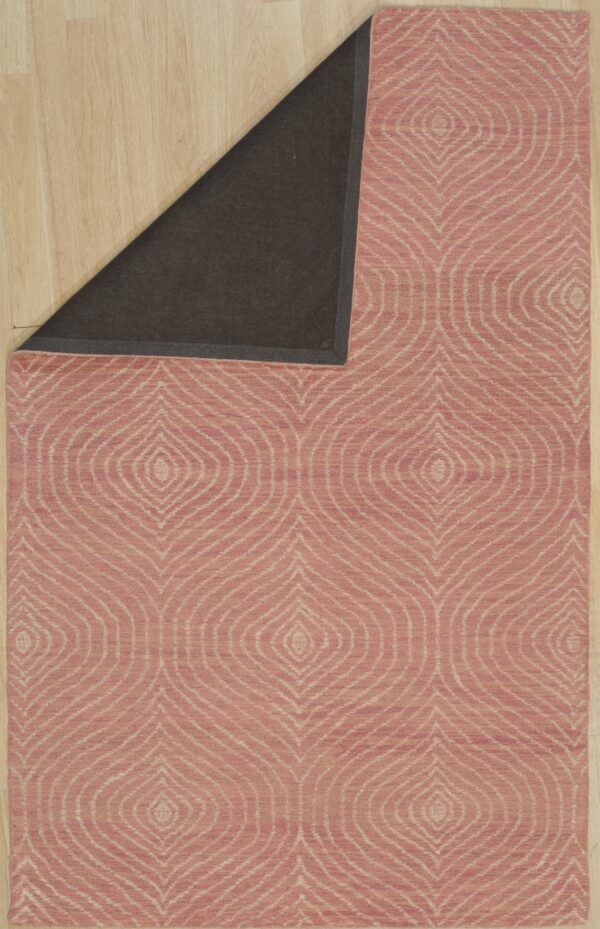 Dusty rose rug with light repeating diamond pattern, folded to show its dark backing on wood planks.