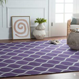 Violet rug featuring a white curved design anchors a bright living room beside a rattan chair on wood flooring.