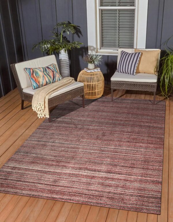 Red and gray striped low-pile rug on a wooden deck between two woven outdoor chairs.