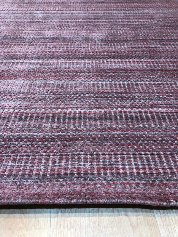 Textured burgundy and gray rug featuring alternating horizontal bands rests on light wood flooring.