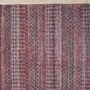 A corner view of a woven red and grey heathered rug with subtle white grid lines on light wood flooring.