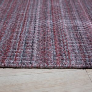 Textured low-angle view of a red and gray heathered rug edge resting on light wood plank flooring.
