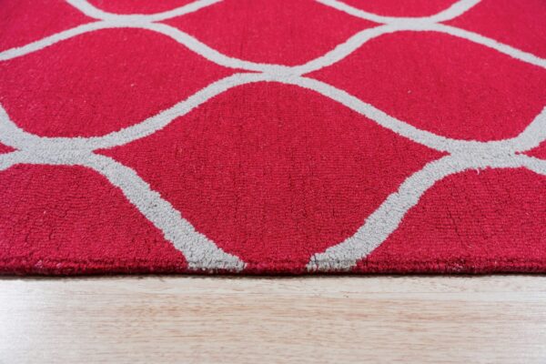 Close-up of a red, medium-pile rug with a gray geometric pattern resting on light wood flooring.