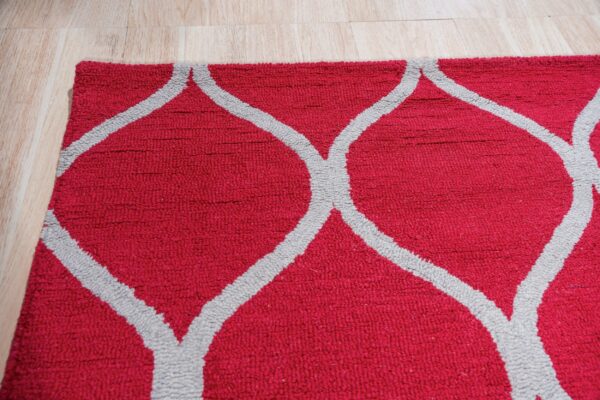 Close view of a textured red rug featuring a gray geometric trellis pattern on a light wood floor.