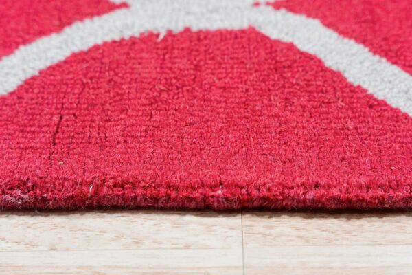 Close-up of a magenta textured rug with gray geometric lines resting on light plank wood flooring.