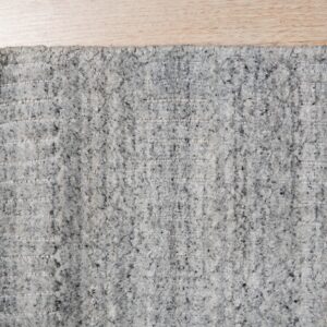 A high-pile gray speckled rug featuring distinct horizontal woven stripes is shown on light wood flooring.