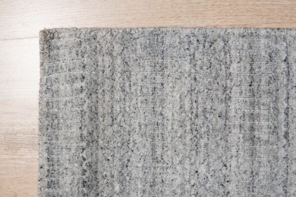 A high-pile gray speckled rug featuring distinct horizontal woven stripes is shown on light wood flooring.