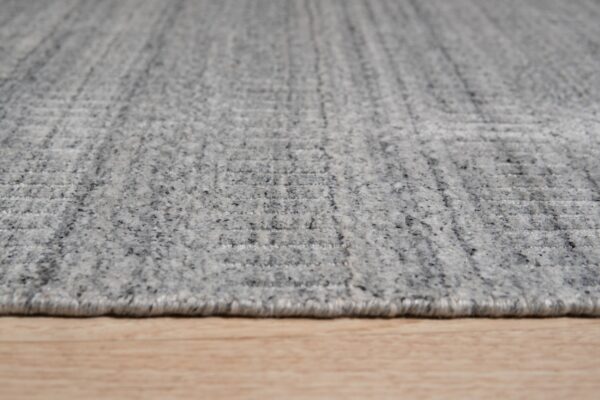 Speckled gray low-pile rug featuring a subtle rectangular pattern rests on light blonde wood flooring.