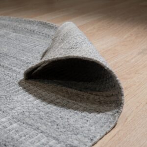 Mottled gray textured rug rolled back on light wood flooring shows the pile and backing.
