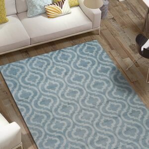 A low-pile blue and light gray trellis patterned rug anchors a white sofa on rustic wood floors.