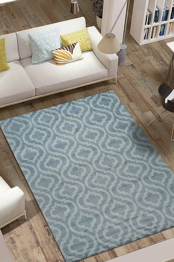 A low-pile blue and light gray trellis patterned rug anchors a white sofa on rustic wood floors.
