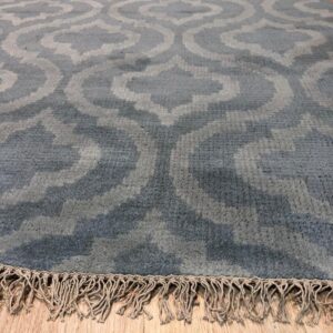 Angled view of a blue and gray trellis rug with natural braided fringe on wood flooring.