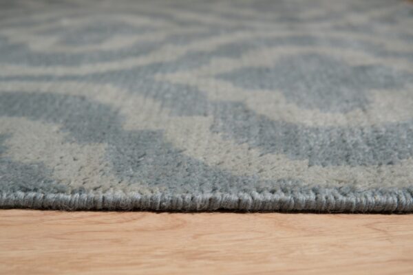 Close-up of a blue and gray high-pile rug edge with an abstract pattern resting on light wood flooring.