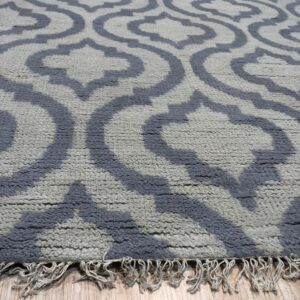 Textured light gray rug with a dark blue interlocking geometric pattern and fringe resting on wood flooring.