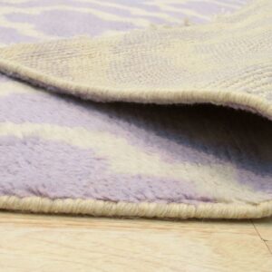 Close-up of a lavender and cream thick pile rug rolled back, showing its woven backing and binding on wood flooring.
