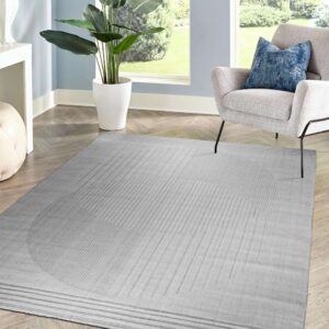 Tonal gray rug with embossed linear patterns sits on herringbone flooring next to a gray armchair and large window.