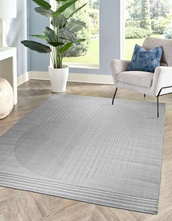 Tonal gray rug with embossed linear patterns sits on herringbone flooring next to a gray armchair and large window.