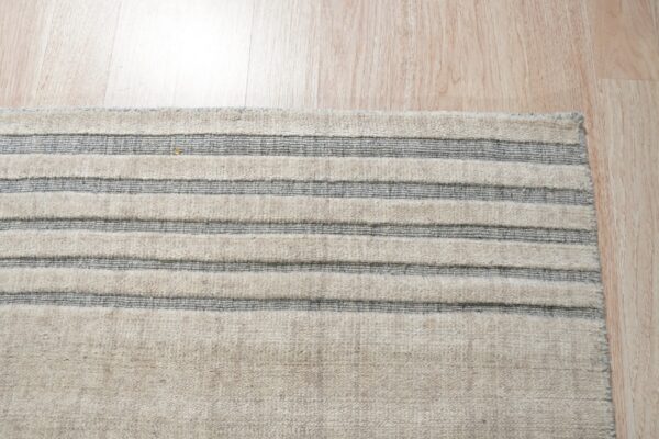 Close-up of a beige rug with raised cream and flat gray horizontal stripes on light wood flooring.