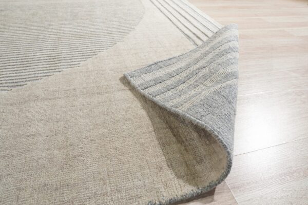 Textured beige rug with subtle gray stripes, partially rolled back on light wood flooring.