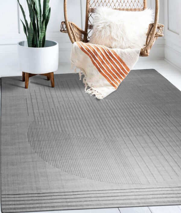 Gray rug featuring subtle embossed vertical stripes forming a large partial circle next to a wicker chair and plant.