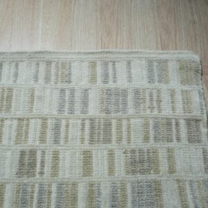 Textured cream rug edge with light gray and beige vertical stripes rests on a light wood floor.