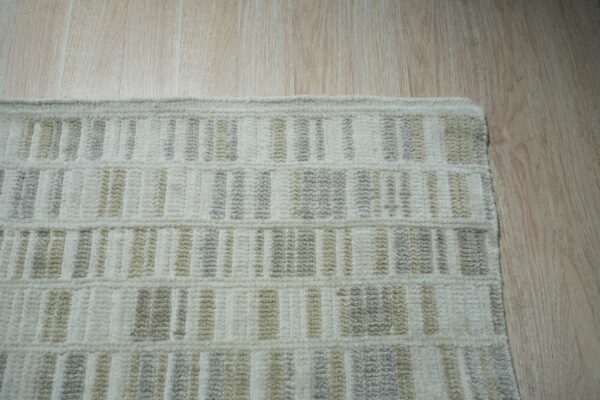 Textured cream rug edge with light gray and beige vertical stripes rests on a light wood floor.