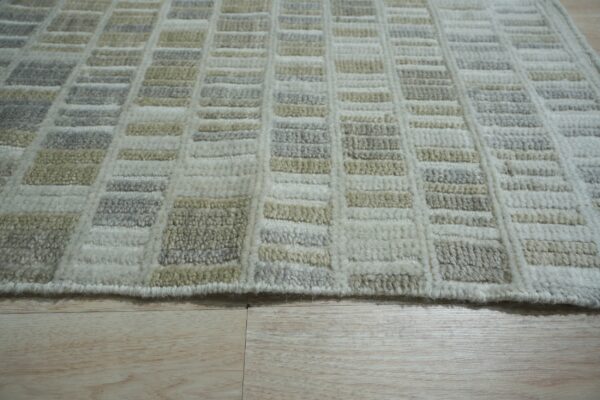 Geometric grid rug in textured cream, pale gray, and beige rests on light natural wood plank flooring.